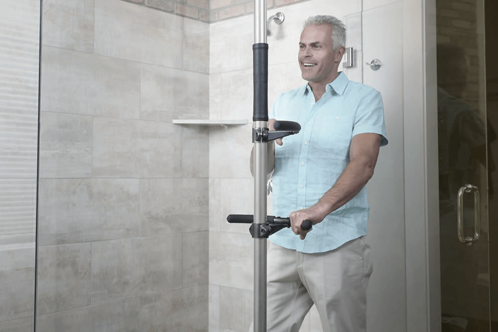 A man is standing in a bathroom holding onto a pole.
