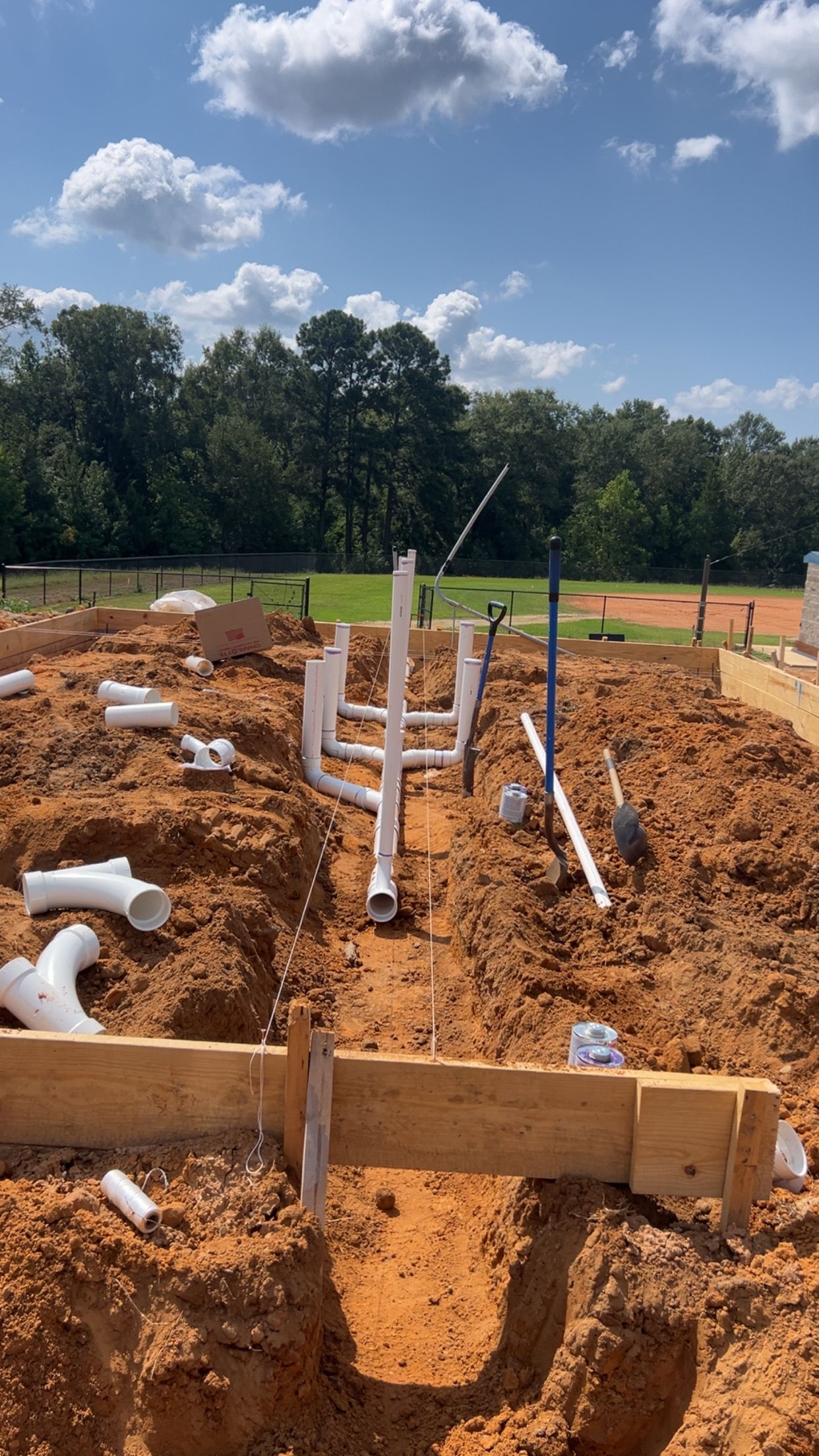 Partly built foundation with wooden forms and white pipes on a dirt lot under a blue sky