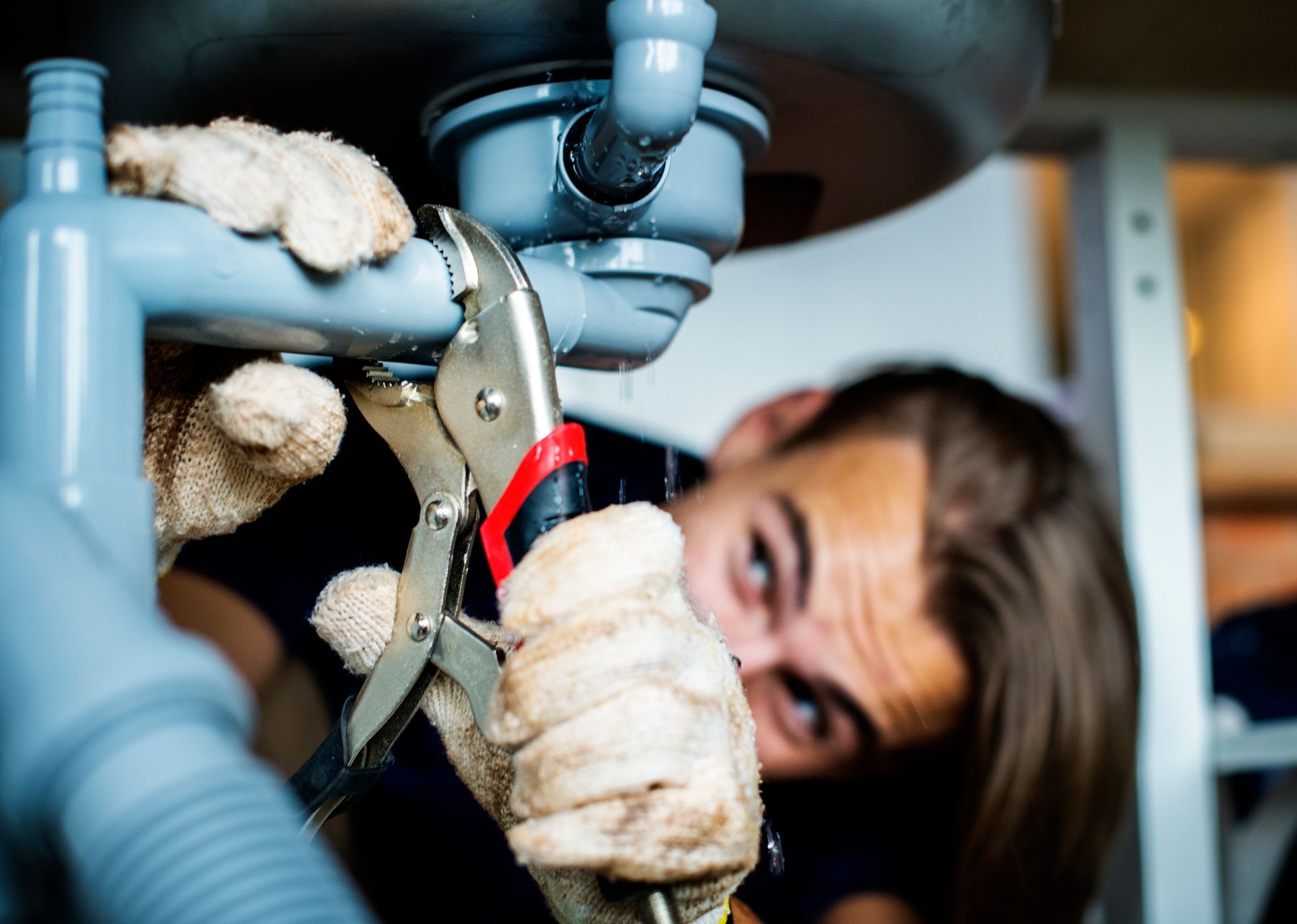 Person using locking pliers to repair plumbing under a sink
