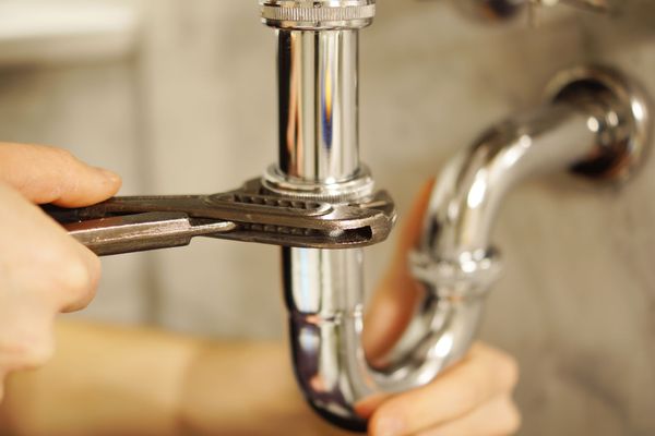 Hand using a wrench to tighten a chrome sink drain pipe under a faucet