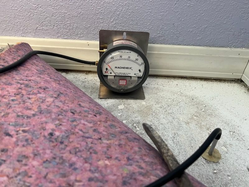 A pressure gauge is sitting on the floor next to a piece of carpet.