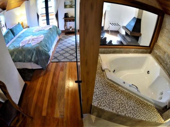 Quarto com piso de madeira, cama e banheiro aberto com banheira de hidromassagem e piso de mosaico.