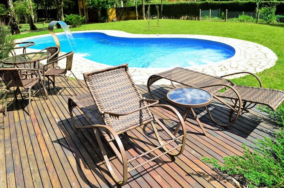 Espreguiçadeiras à beira da piscina em um deck de madeira ao lado de uma piscina azul curva.
