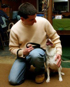 A man is kneeling down next to a dog with its mouth open