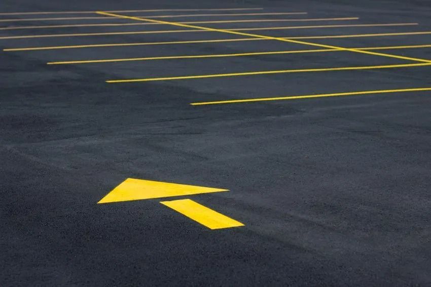 Orange traffic cone in a newly painted parking space, with yellow lines on asphalt, houses in the background.