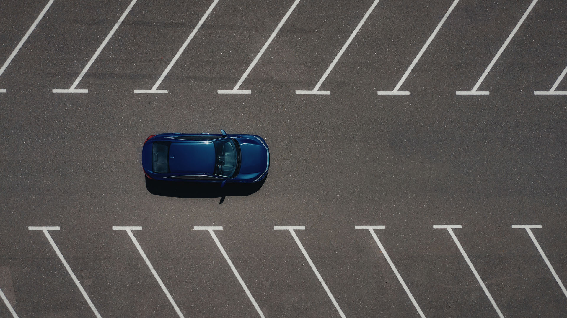 Newly paved black asphalt driveway in front of a blue-gray house with a white garage door, yellow markings, and a white sign.