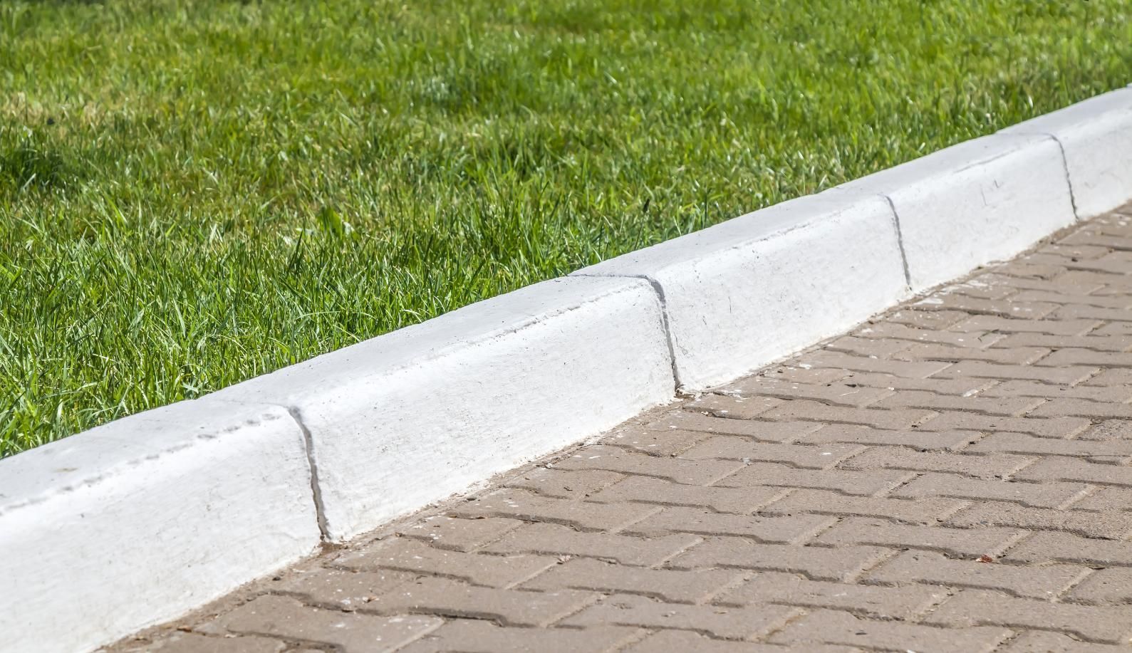 Concrete curb separating a brick paved sidewalk from a grassy lawn.