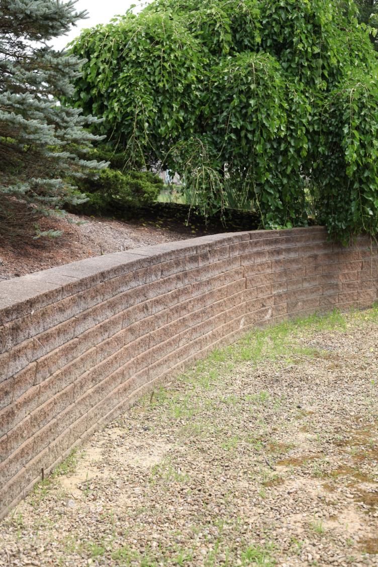 Curved, tiered retaining wall in a yard, with green trees in the background.
