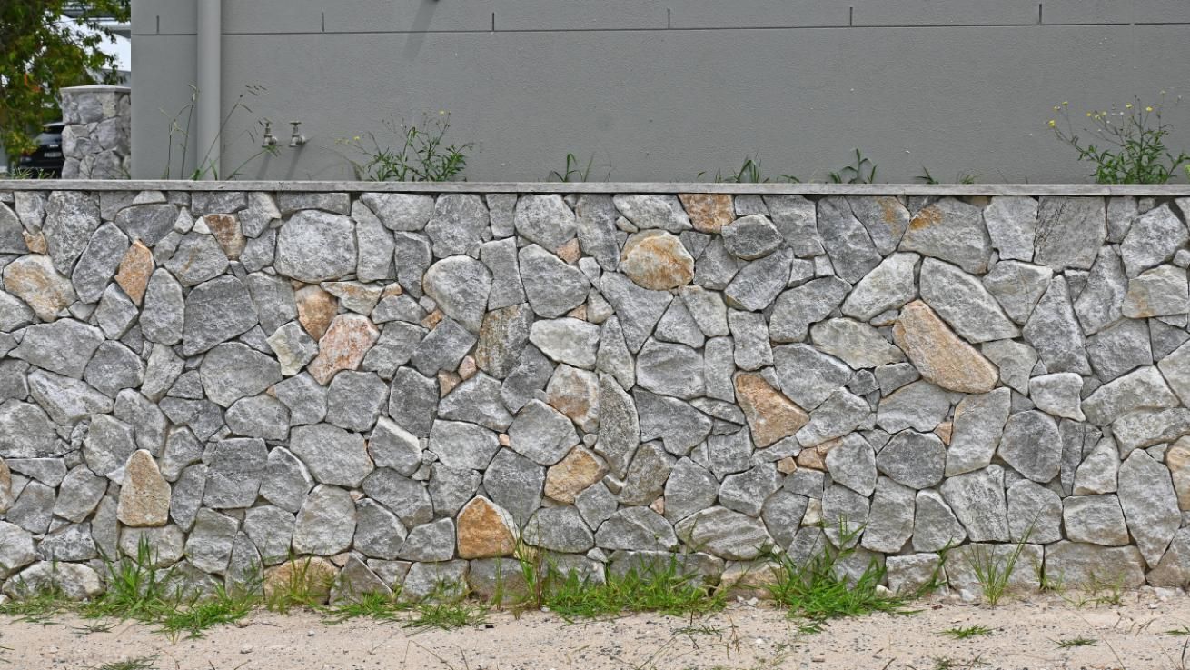Stone wall with gray and tan rocks; concrete top, grass at base.