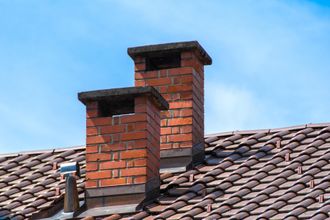 Two red brick chimneys on a tiled roof against a blue sky.