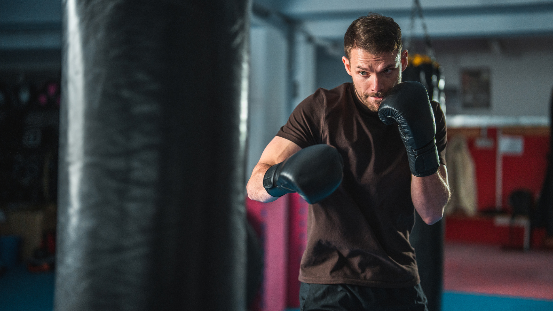 A focused male boxer in a gym throws a jab at a heavy bag during a training session. He is wearing b