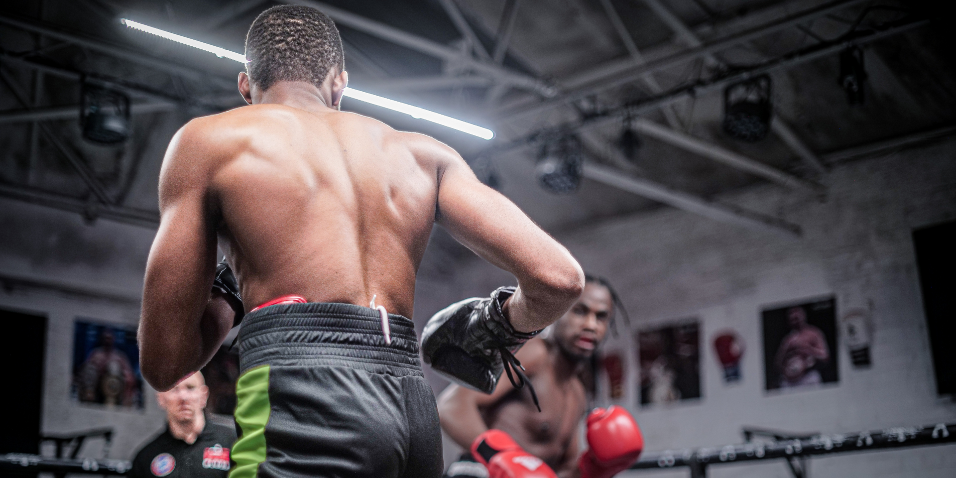 Boxers sparring in a ring. One faces away, other throws a punch. Referee watches.