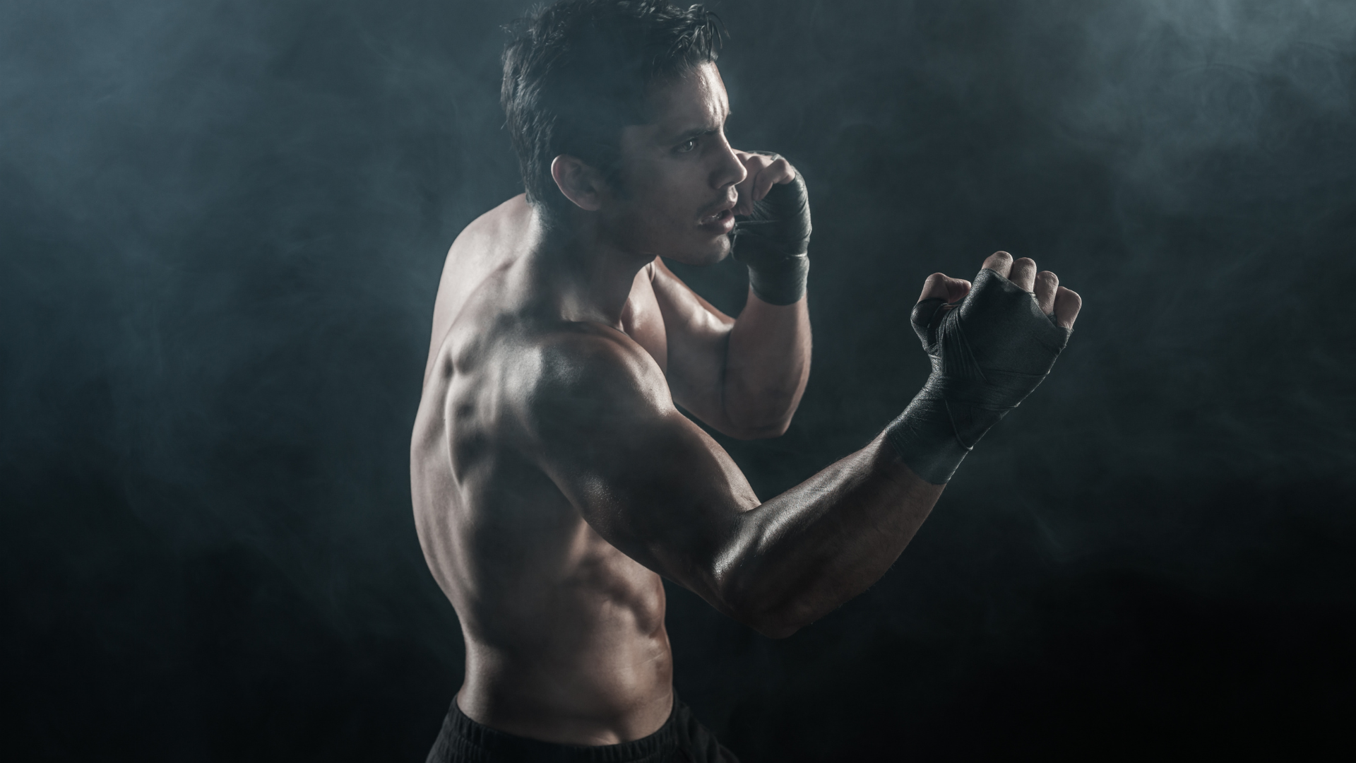 Shirtless boxer in gloves shadowboxing in a smoky dark studio