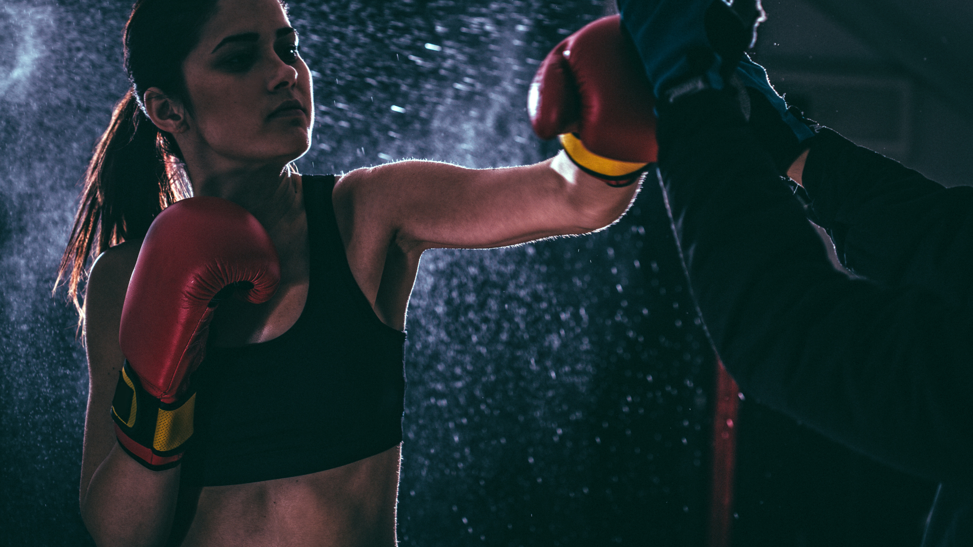 A woman training boxing in a dark place with water moist bg