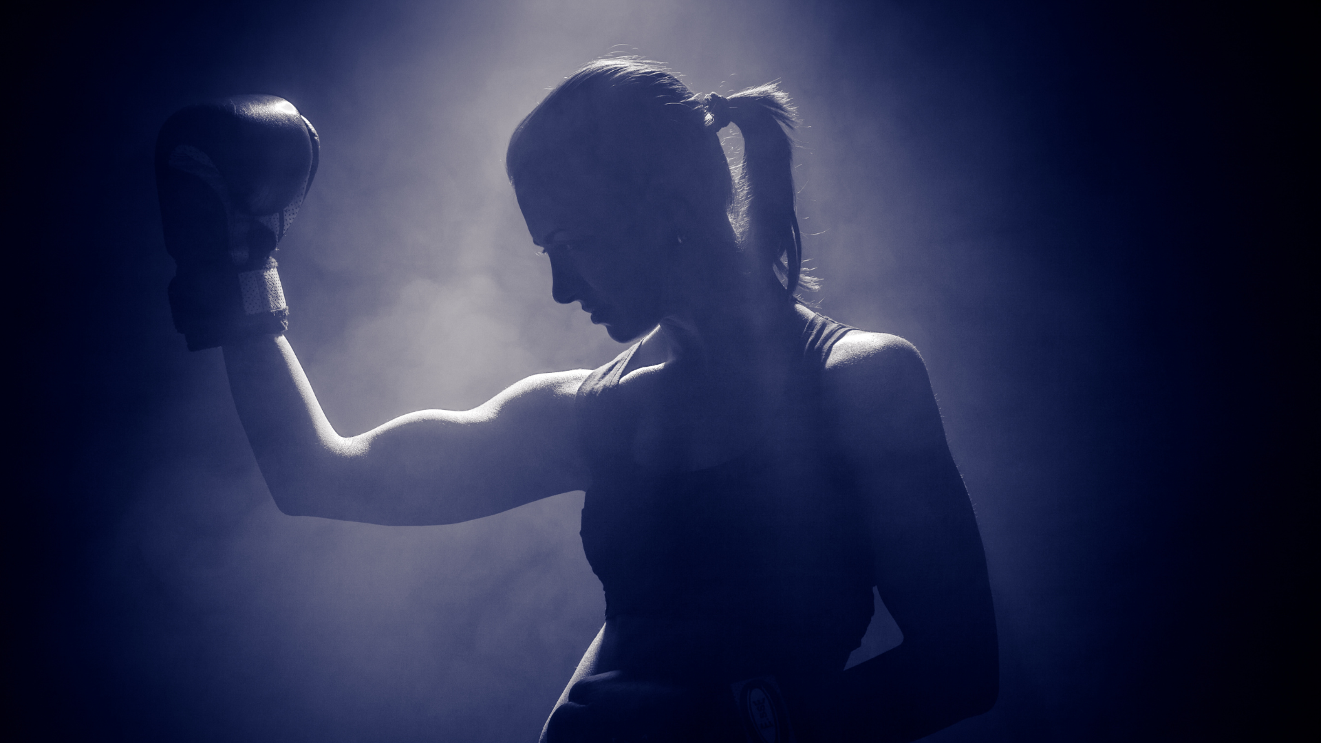 A silhouette of a woman wearing boxing gloves in a dark room.