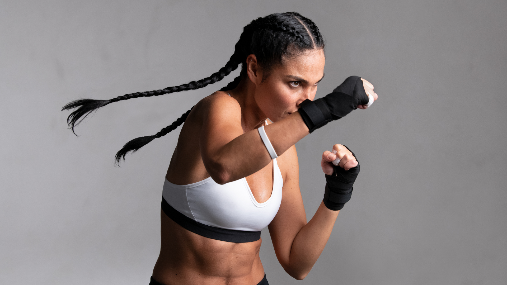 A woman in a white sports bra and black shorts is boxing.