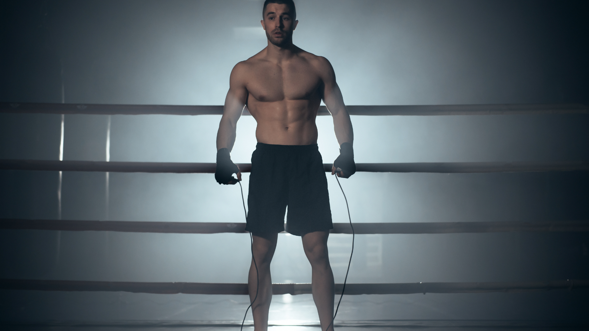 A shirtless man is jumping a jump rope in a boxing ring.