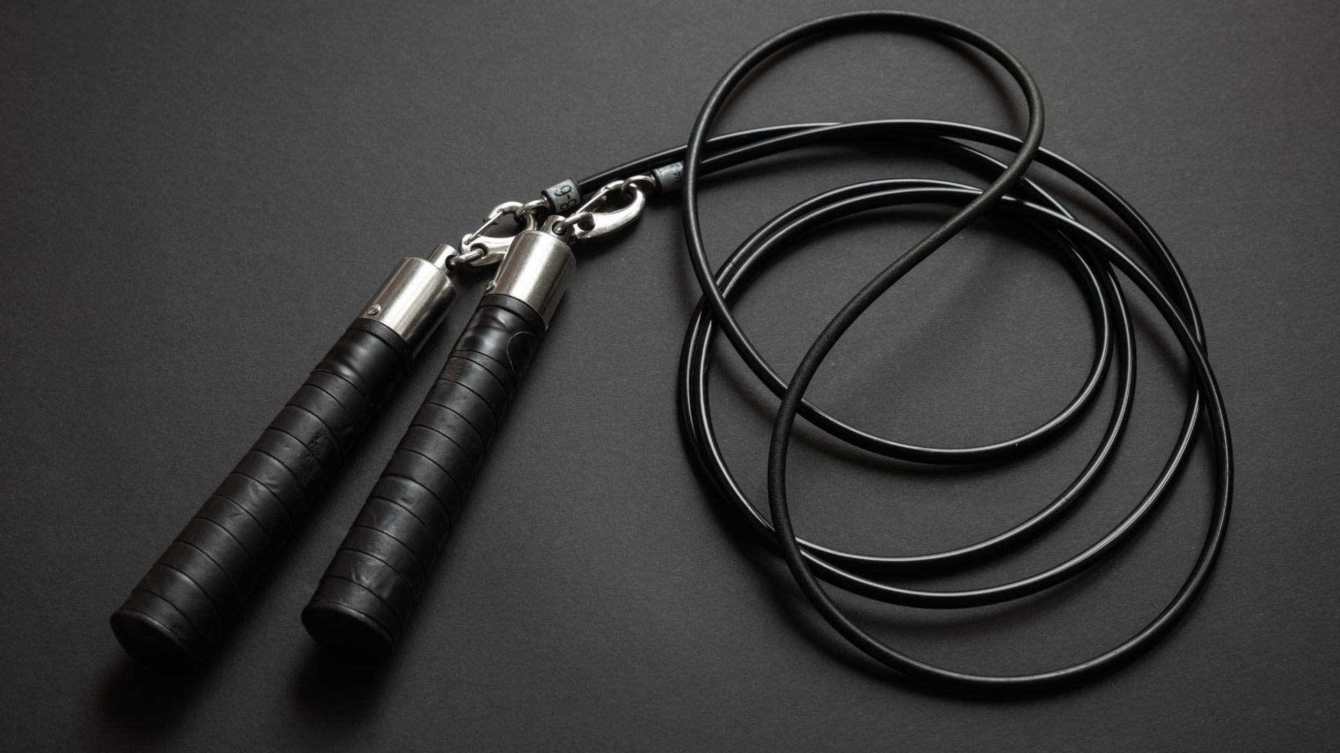 A black jump rope with silver handles on a black surface