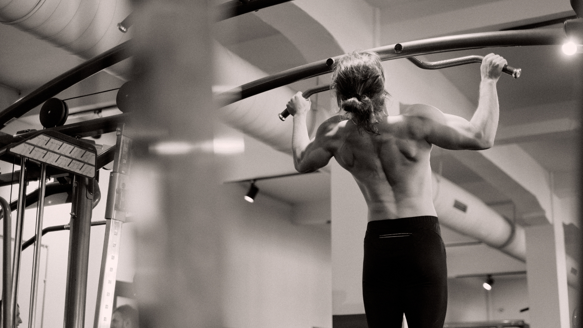 Man doing a pull-up in a gym, back exposed, gripping a bar.
