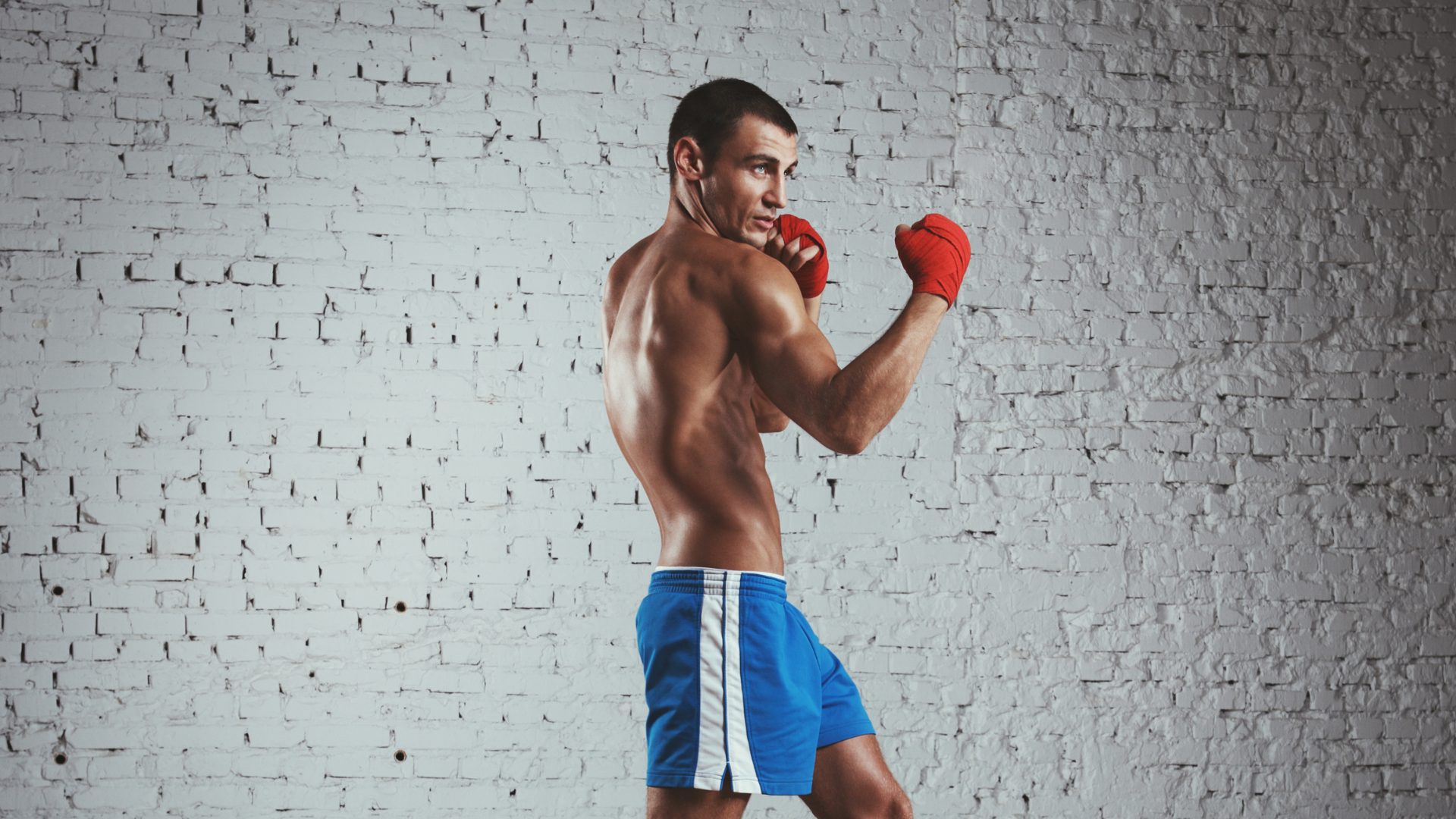 A man wearing boxing gloves is standing in front of a white brick wall.