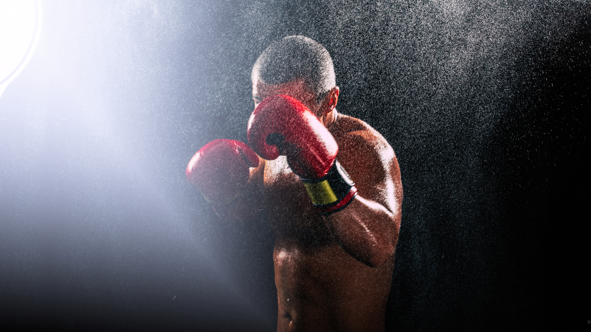 A man wearing boxing gloves is standing in front of a white brick wall.