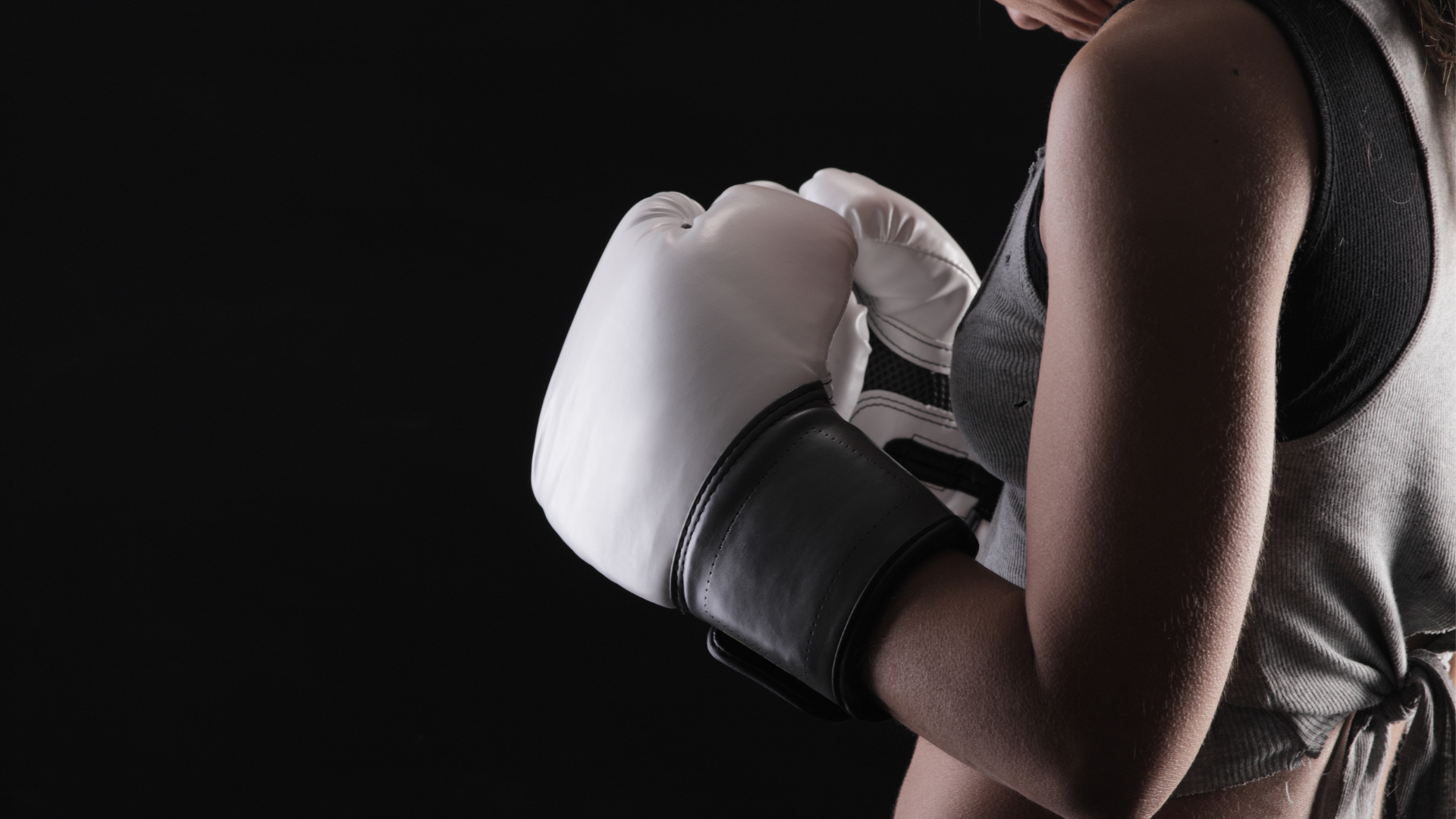 Boxer in black gloves punches a red heavy bag. Dark gym setting.