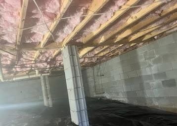 Basement with exposed pink insulation, metal support posts, cinder block walls