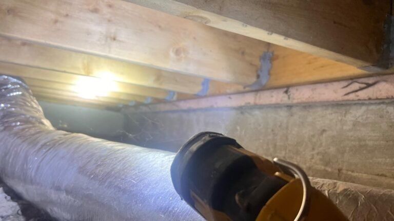 Attic crawlspace with exposed wooden joists, a bright bulb, and insulated ducting