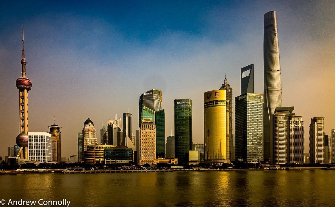 Shanghai skyline with iconic Oriental Pearl Tower and modern skyscrapers reflecting in the river.