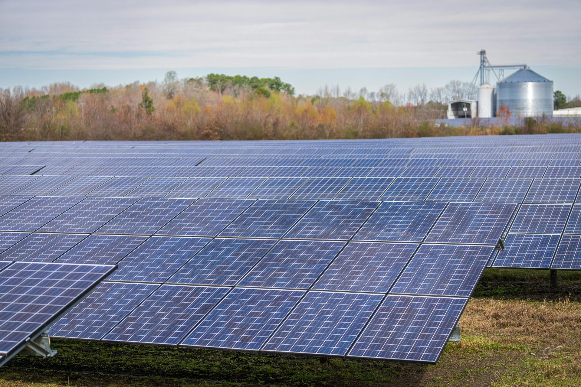 Solar panels in field with silo and trees in the background.
