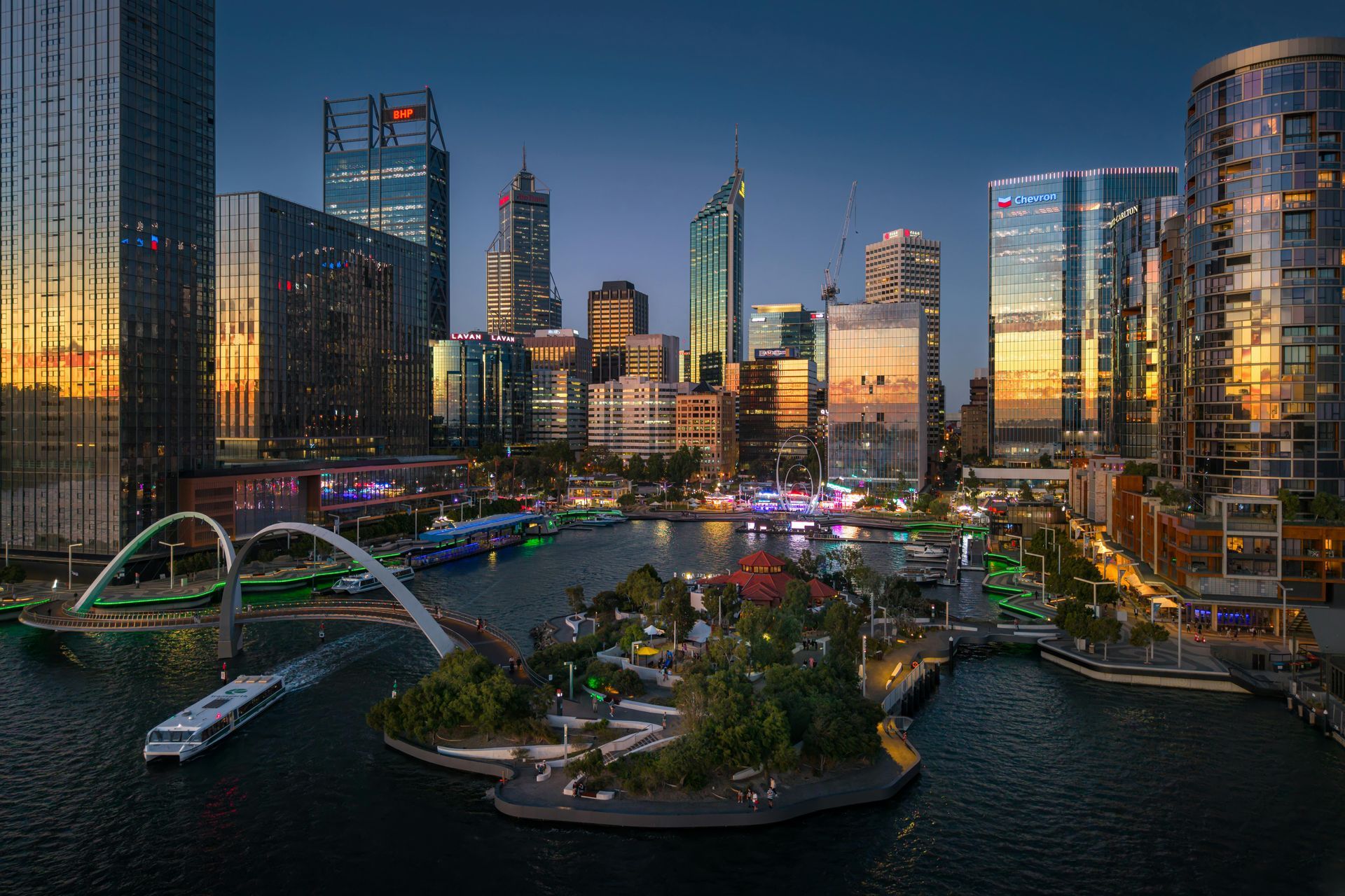 Pity skyline at dusk, featuring illuminated skyscrapers, a bridge, and boats on the water.c
