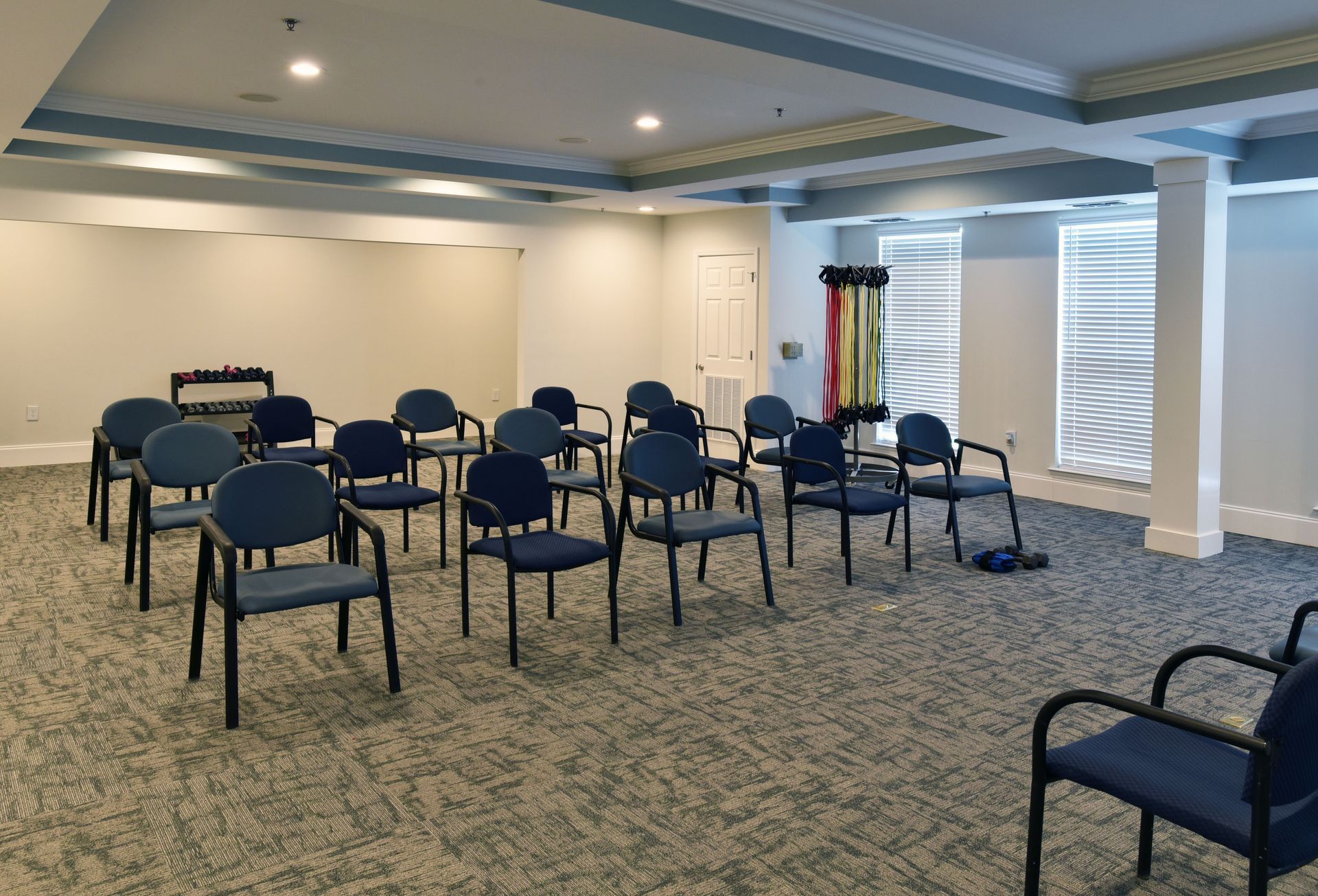 Bright meeting room with rows of blue and beige chairs, wall mirror, ceiling fans, and large windows