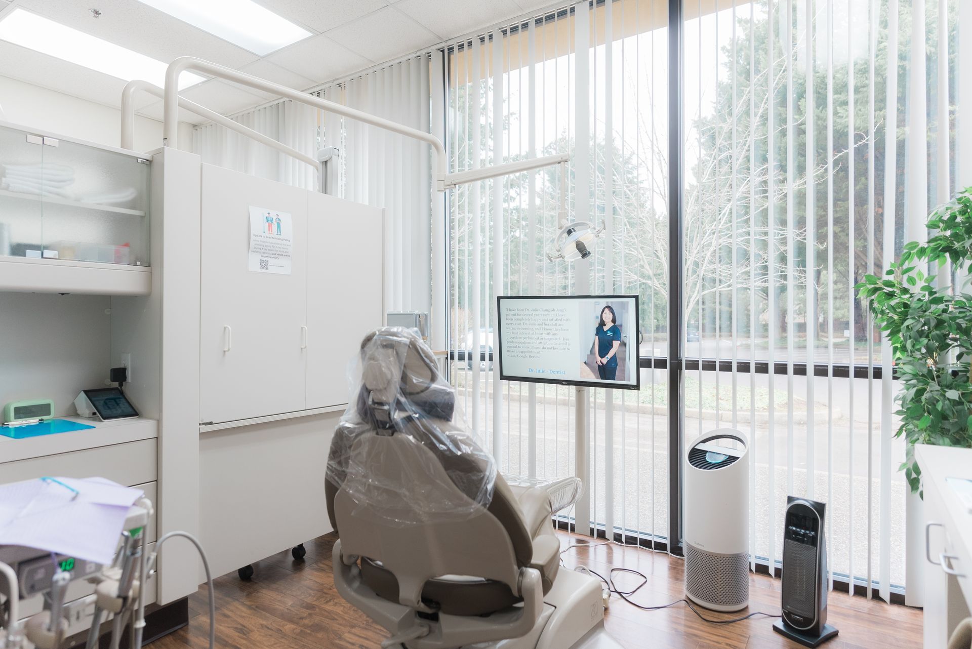 A woman is smiling while sitting in a dental chair next to a dentist.