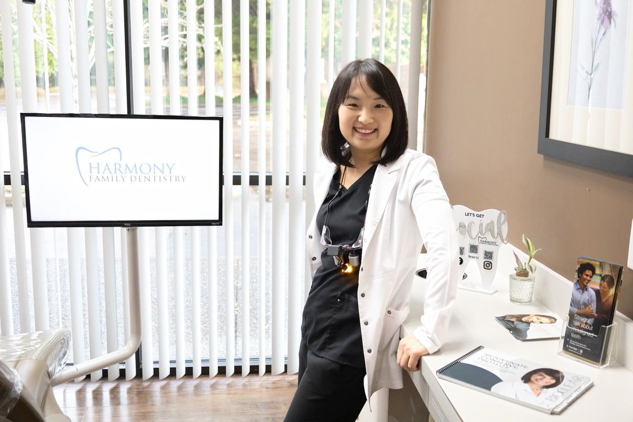A woman is smiling while sitting in a dental chair next to a dentist.