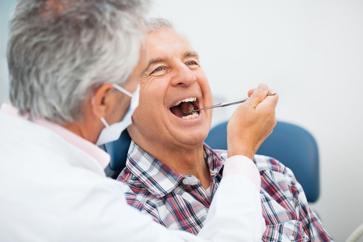 A woman is smiling while sitting in a dental chair next to a dentist.