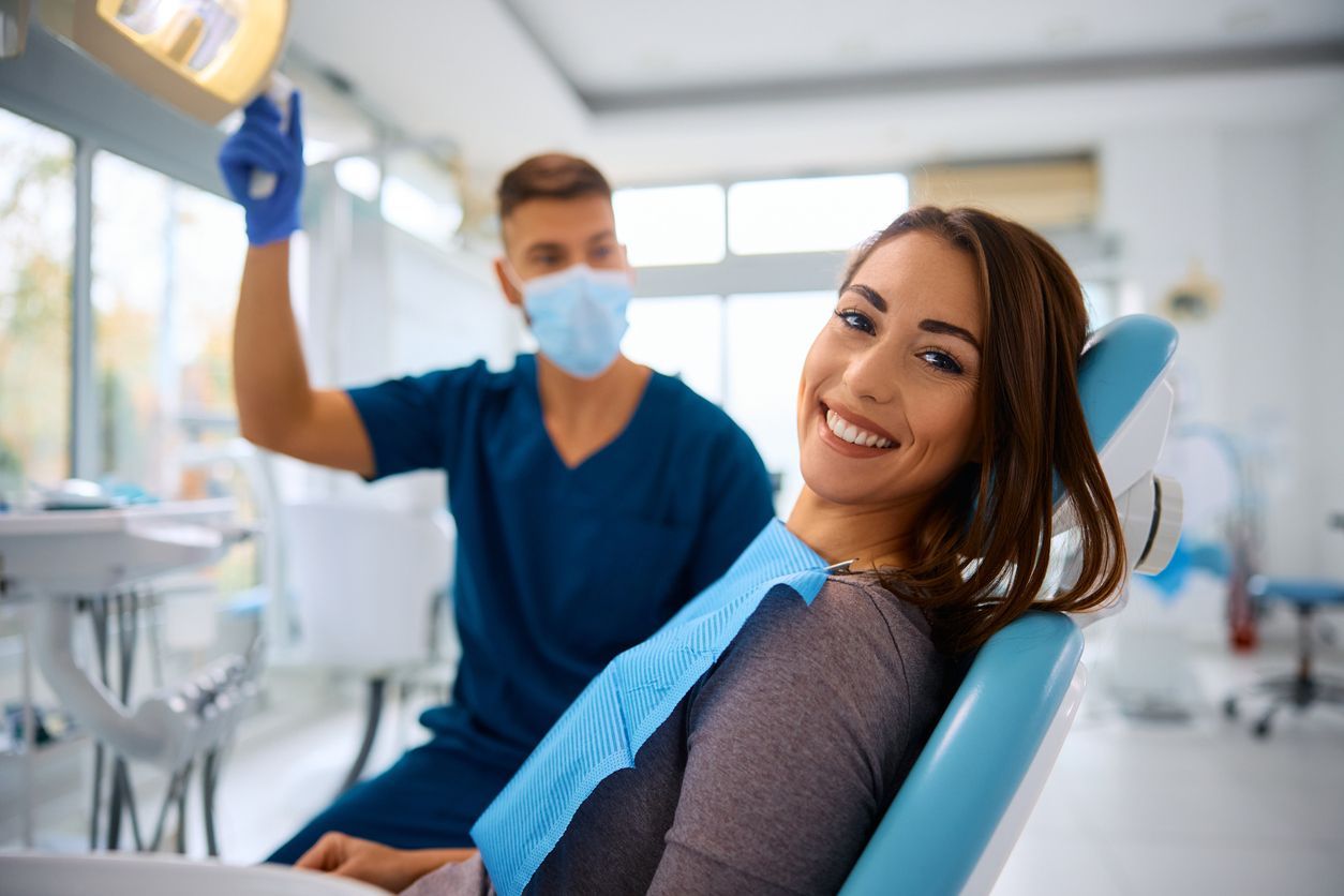 A woman is sitting in a dental chair with a dentist in the background.