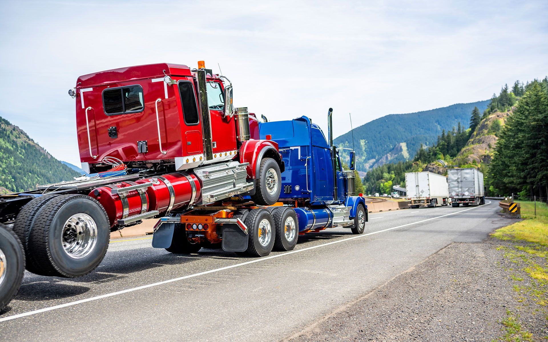 A red semi truck is driving down a highway next to a blue semi truck.