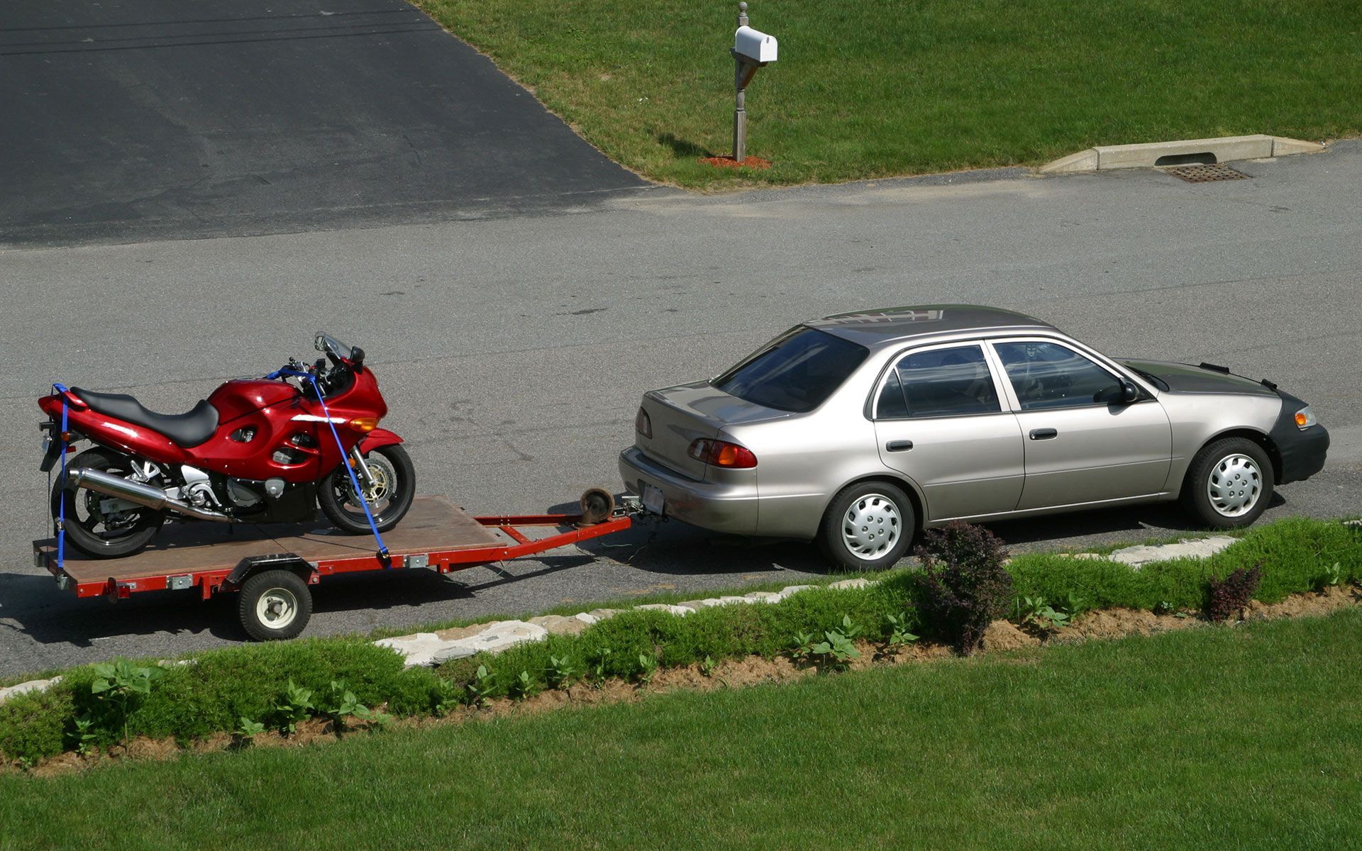 A silver car is towing a red motorcycle on a trailer
