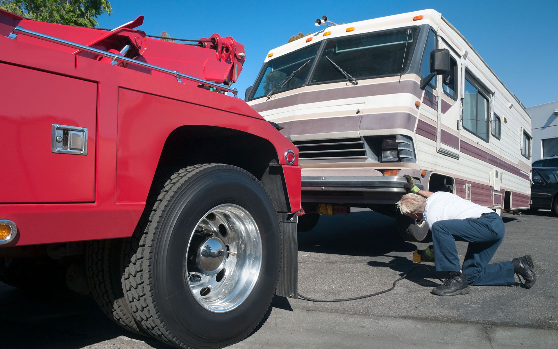 A man is working on a rv that is being towed by a tow truck.