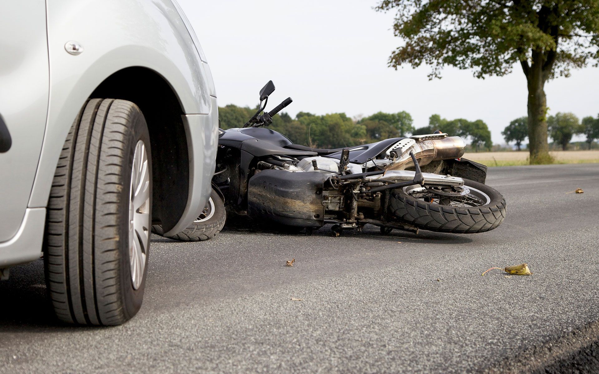 A motorcycle has crashed into a car on the side of the road.