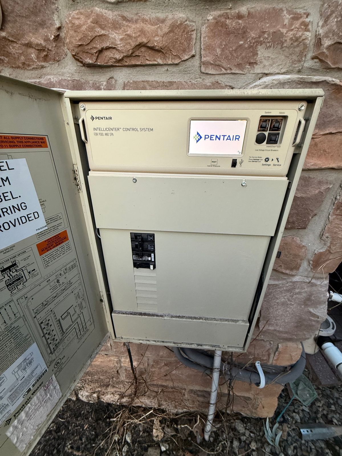 A electrical box is sitting on the ground next to a brick wall.