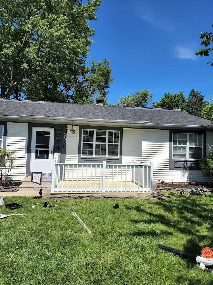 White and gray house with small deck, green lawn, and blue sky.