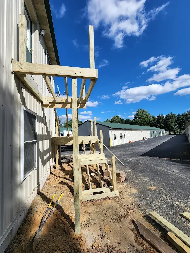 Wooden deck and staircase under construction next to a building on a sunny day.