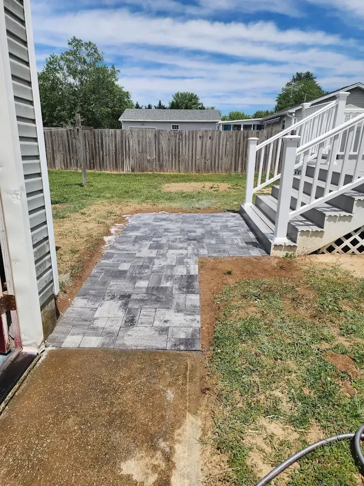 Paver walkway alongside a house and steps. Gray pavers lead to white stairs, with grass and a fence in the background.