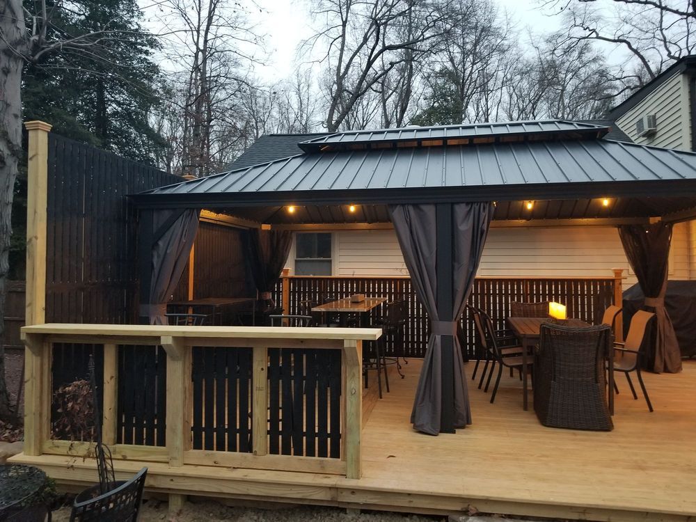 Wooden deck with a covered outdoor dining area, gray curtains, and tables/chairs.