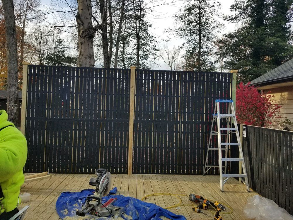 A partially built black bamboo fence on a wooden deck; a person and tools are visible.