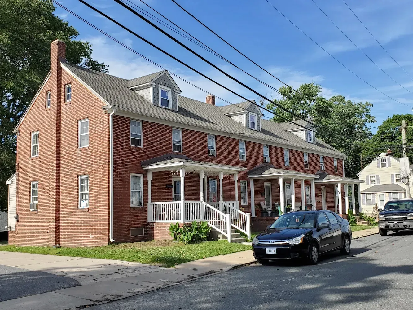 Brick apartment building with white porches, parked cars on street, blue sky.