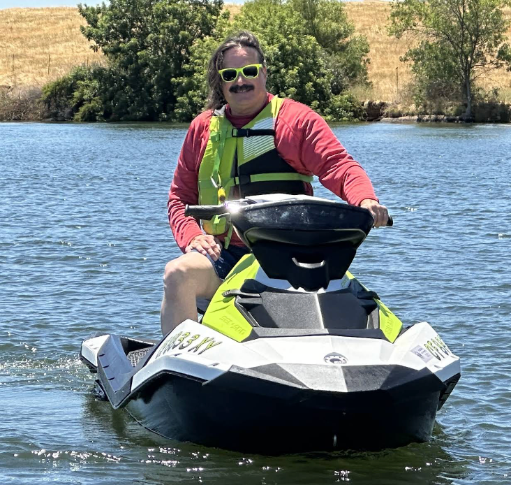 A person in a red long-sleeved shirt and lime green life vest riding a white and black jet ski on a lake.