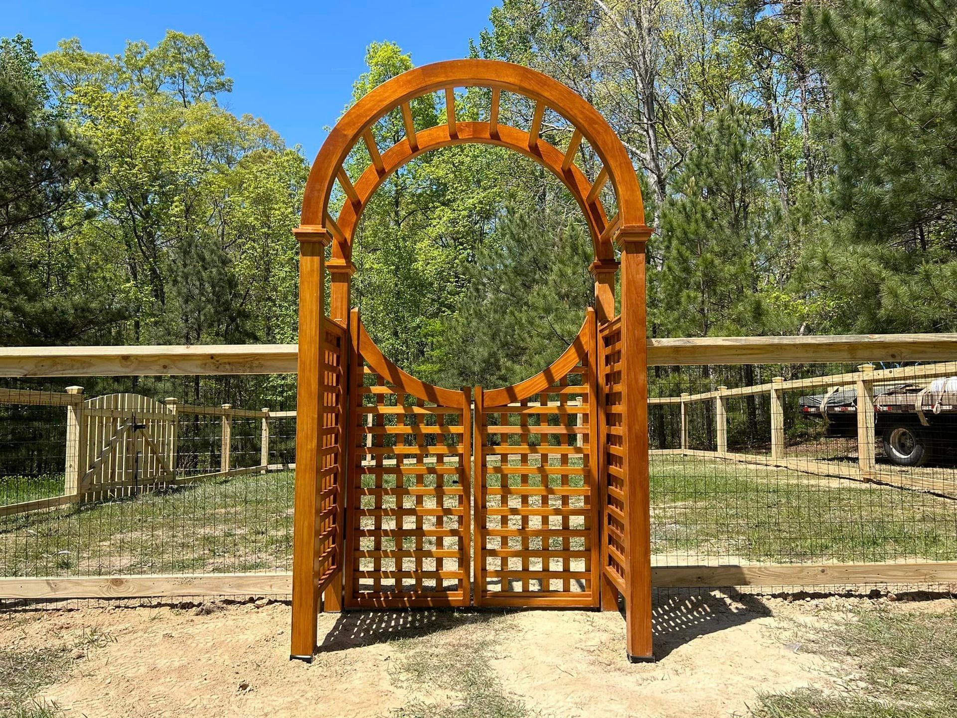 A wooden archway with a fence in the background and trees in the background.