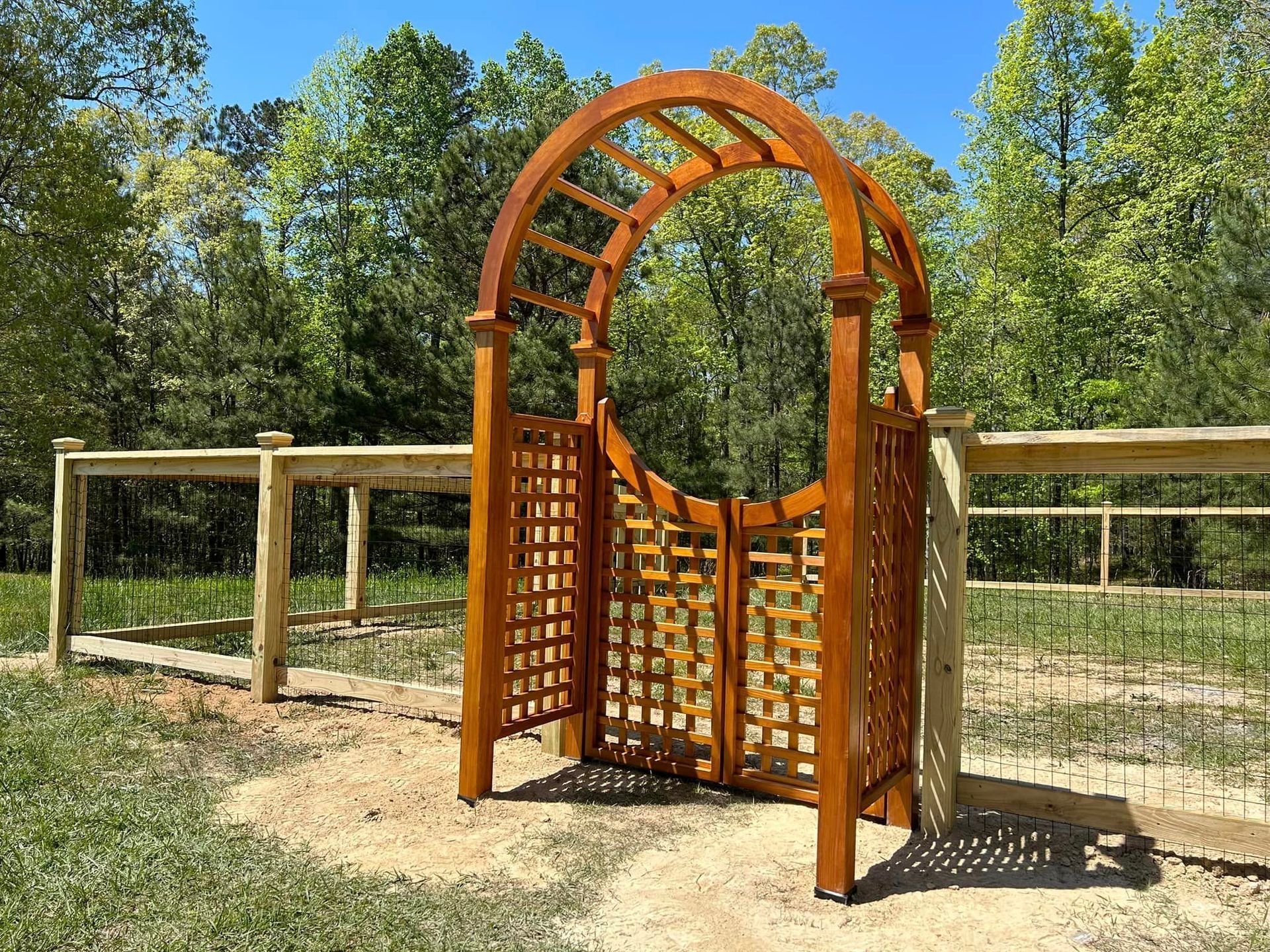 A wooden archway with a gate in the middle of a field.